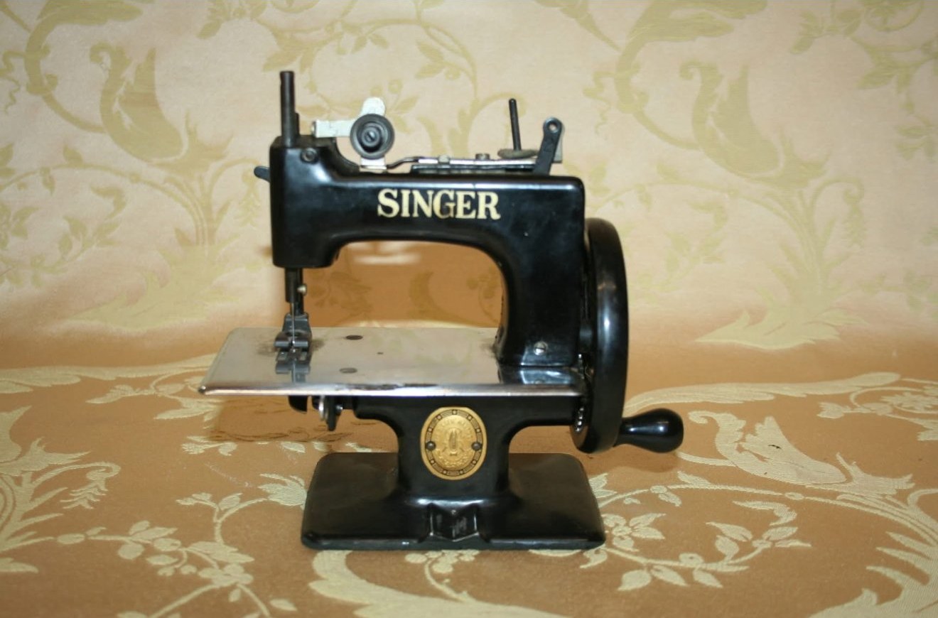 A miniature black Singer hand-crank sewing machine on a damask cloth