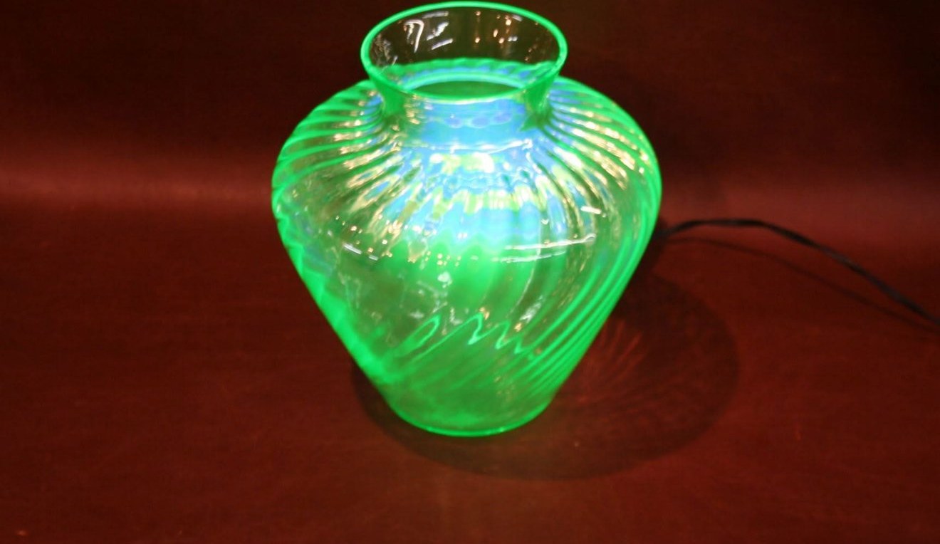 A swirled uranium-glass vase glowing bright green under ultraviolet light