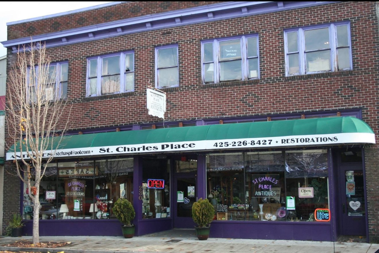 The brick storefront of St. Charles Place Antiques & Restorations on Wells Avenue South — purple-painted trim, a green awning lettered in cream, and display windows full of pieces